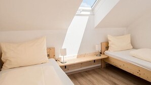 A small, modern room with two beds, a skylight, and a wooden bench.