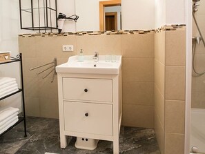 Une salle de bain avec un lavabo blanc, deux tiroirs, un porte-serviettes et un espace douche.