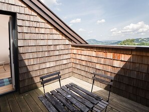 Une terrasse en bois avec deux bancs et une porte vitrée donnant sur un espace intérieur.
