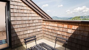 Una terraza de madera con dos bancos y un ventanal de vidrio que da a un espacio interior.