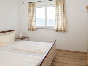 Een slaapkamer met een bed, een nachtkastje, een raam met gordijnen en uitzicht op de omgeving.