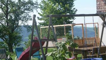 Une terrasse en bois avec un portique, un toboggan et une balançoire suspendue.
