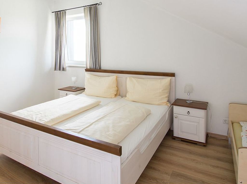Une chambre à coucher avec un lit en bois, deux tables de chevet, une commode, une fenêtre avec des rideaux et une chaise.