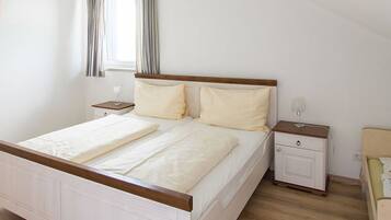 Une chambre à coucher avec un lit en bois, deux tables de chevet, une commode, une fenêtre avec des rideaux et une chaise.