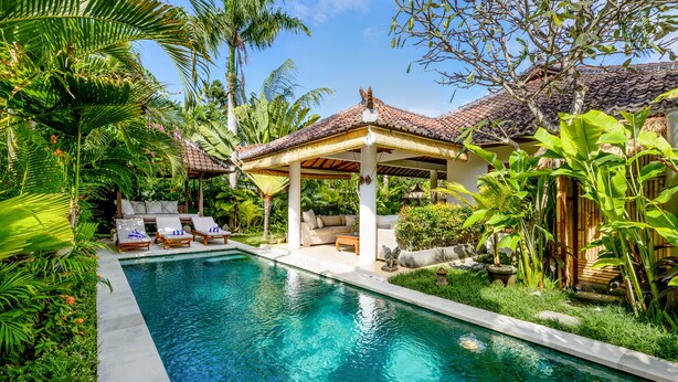 A pool area with lounge chairs, a covered seating area, and lush tropical vegetation. - Villa Vitari (Seminyak)