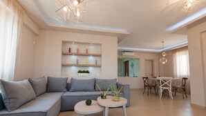 A modern living room with a grey sofa, two small tables, and a dining area with a white table and chairs. - Harmony of Nature villa (Rethymno)