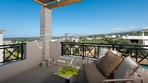 A balcony with a view of a town, a table with a pitcher and glasses, and a sofa with cushions. - Harmony of Nature villa (Rethymno)