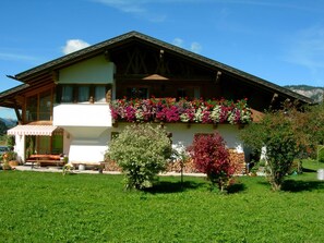 Una casa de dos pisos con balcón, terraza de madera y jardín.