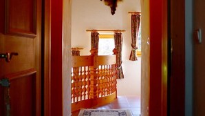 Un passadís amb una porta de fusta a l'esquerra, una catifa amb dibuixos, un banc de fusta amb cortines i un lluminari al sostre.