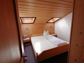 Una habitación con techo de madera, una cama con colchón blanco, dos mesitas de noche y una pequeña cómoda.