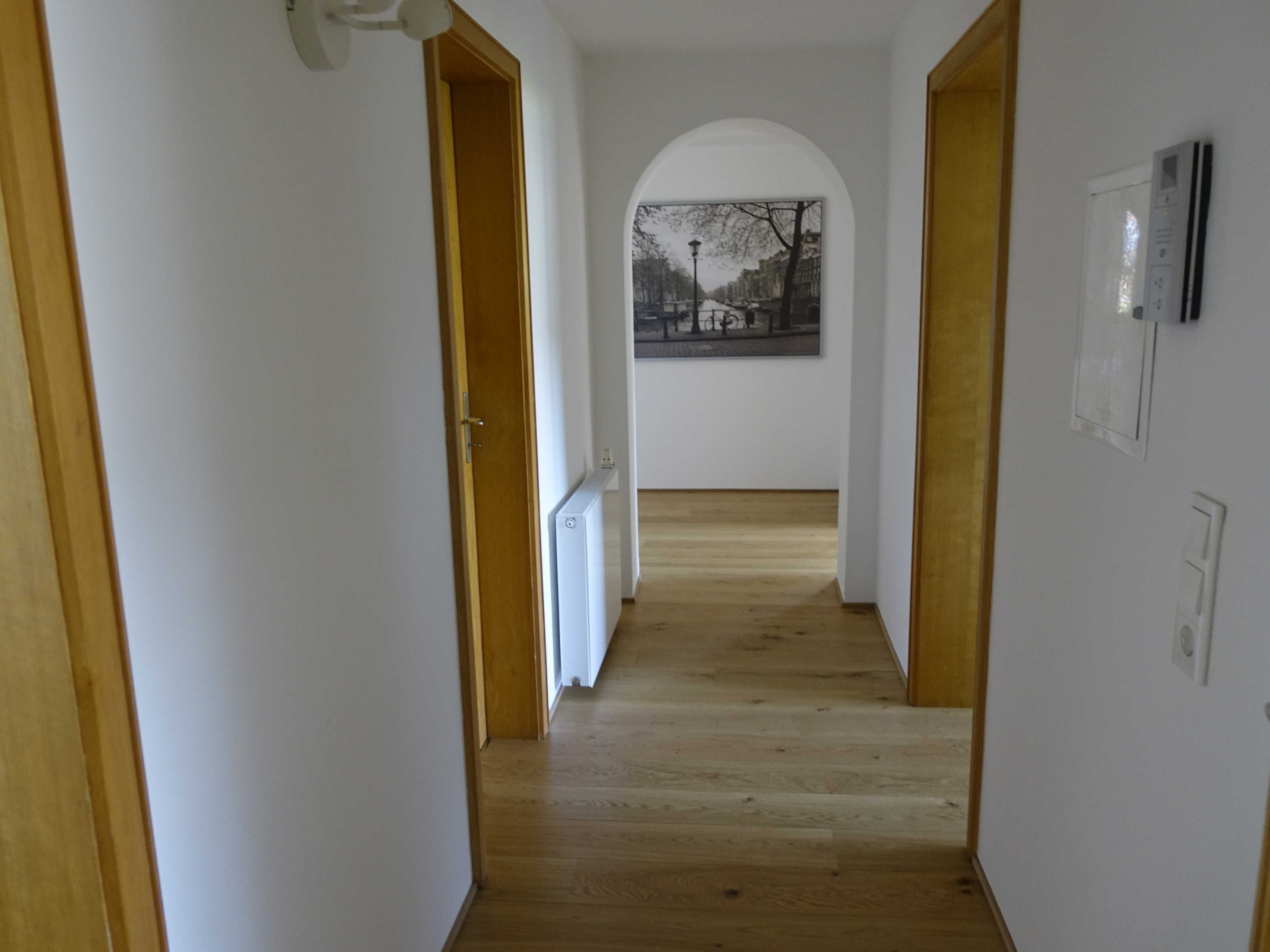 Ein Korridor mit Holzboden, weißen Wänden und einem Rundbogenfenster am Ende.
