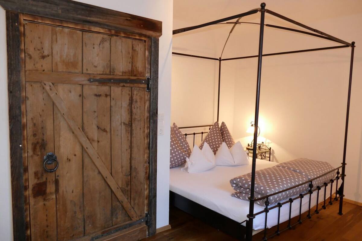 Een slaapkamer met een hemelbed, een houten deur en een nachtkastje met een lamp.