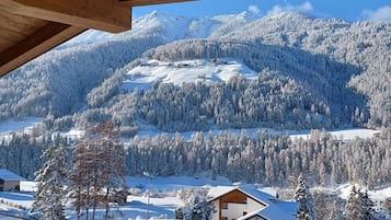 Une vue depuis un balcon en bois donnant sur un paysage enneigé, avec des montagnes en arrière-plan et une route au premier plan.