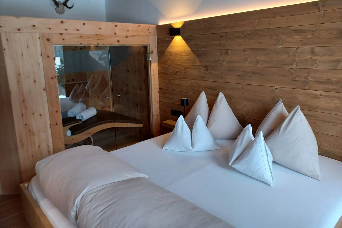 Een moderne slaapkamer met een houten hoofdbord, een badkamer met glazen wanden en een bed met witte lakens en kussens.