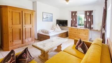 Un salon avec un canapé jaune, un meuble en bois, une télévision et une fenêtre avec des rideaux.