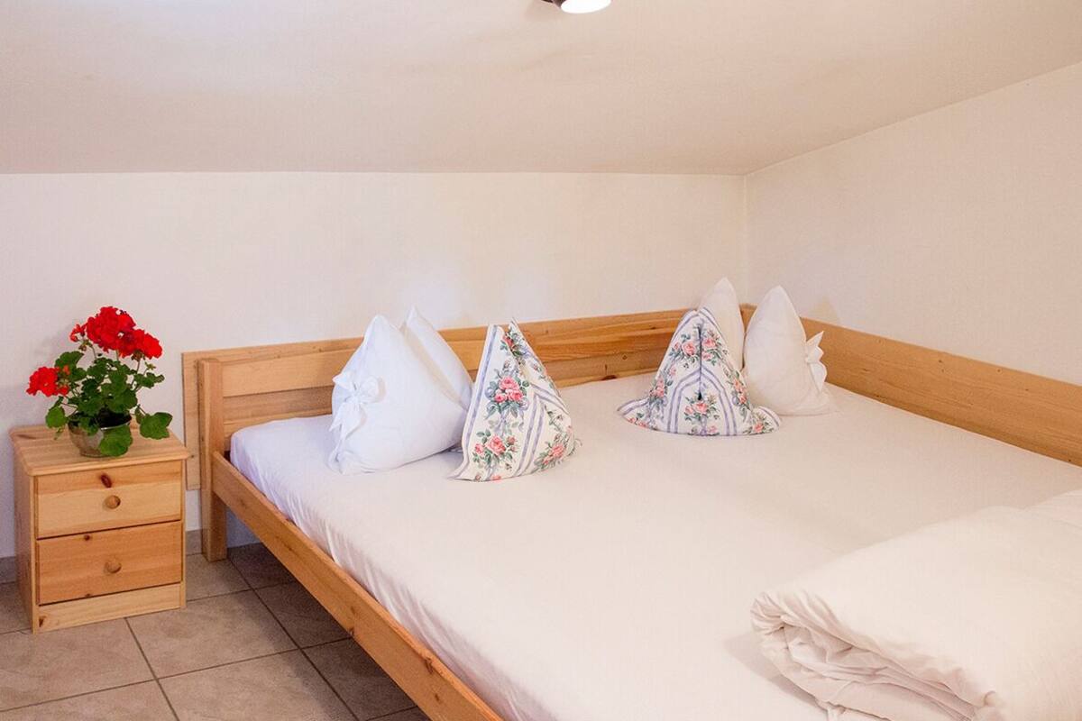 Een enkel bed met een houten hoofdbord, een nachtkastje met een bloemenvaas, en een effen muur.