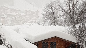 Een houten chalet, deels bedekt met sneeuw, met een zichtbaar raam en een trap die omhoog leidt.
