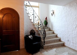 Eine Treppe mit schmiedeeisernem Geländer, eine Holztür, ein schwarzer Ledersessel und ein kleiner Blumentopf.