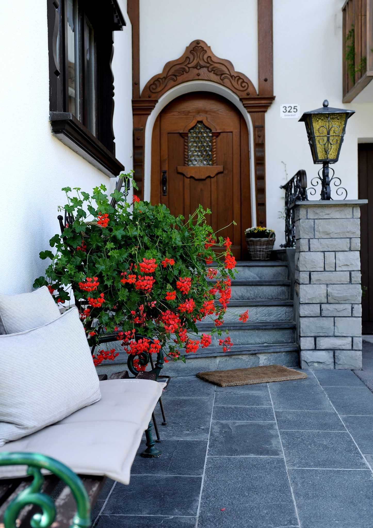 A building entrance with a wooden door, steps, a stone wall, a bench, and a potted plant with red flowers.