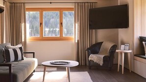 Ein Wohnzimmer mit Sofa, Sessel, Couchtisch und einem an der Wand befestigten Fernseher.