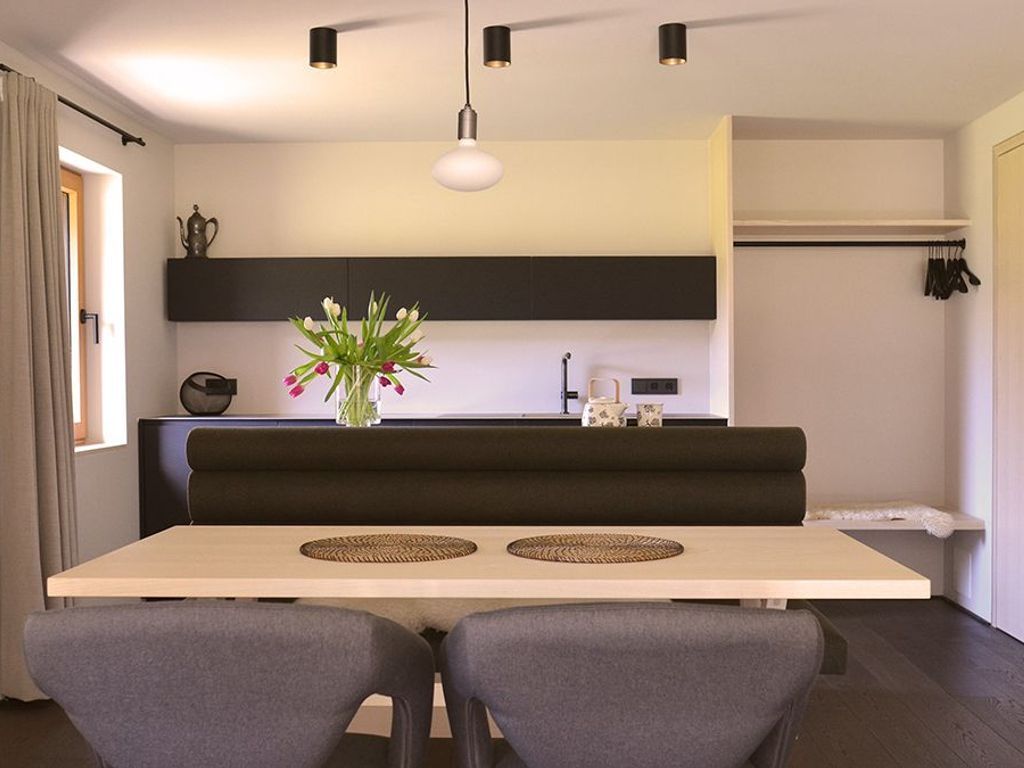 Una cocina moderna con comedor, un sofá negro y un jarrón con flores.