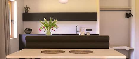 Una cocina moderna con comedor, un sofá negro y un jarrón con flores.
