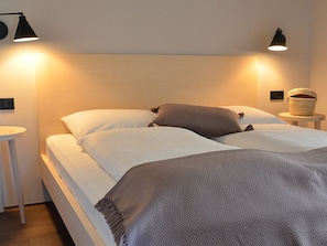 Ein Doppelbett mit gemustertem Überwurf, zwei Nachttischlampen, ein kleiner runder Tisch und ein Korb auf dem Nachttisch.