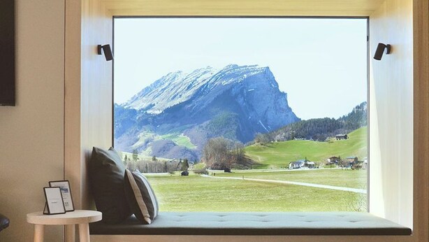 Ein Zimmer mit großem Fenster und Blick auf einen Berg und eine grüne Landschaft.