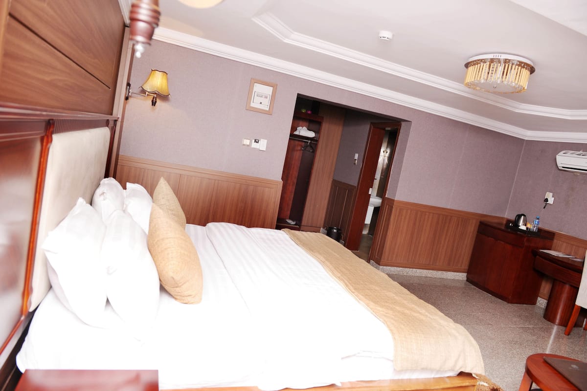 A hotel room with a bed, bedside table, lamp, and a desk with a chair.