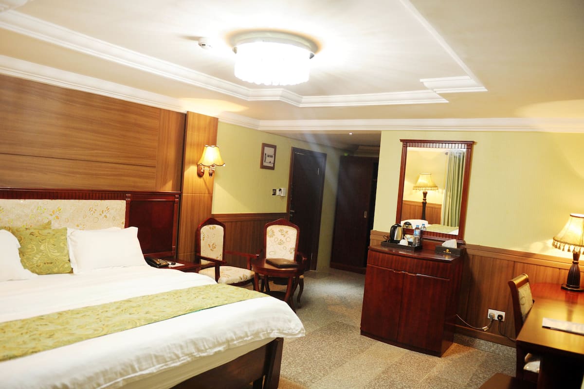A hotel room with a bed, a desk, a chair, a mirror, and a lamp.