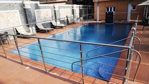 A rectangular swimming pool with a tiled deck and metal railings. - R&A City Hotel (Lagos)