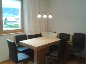 Comedor con mesa de madera y seis sillas. Se ve una ventana con cortinas y vistas a casas.