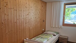 A room with two single beds, wooden panel walls, a ceiling fan, a window with curtains, and a small bedside table. - Apartment Simone - Apartment Simone (Schoppernau)
