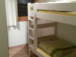 A bunk bed with a ladder, a window with curtains, and a patterned bedspread.