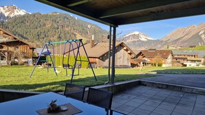 A patio with a table and chairs, a swing set, and a view of mountains. - Apartment Simone - Apartment Simone (Schoppernau)
