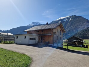Una casa de madera con garaje, un porche cubierto y montañas al fondo.