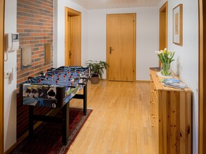 A room with a foosball table, a wooden cabinet with magazines, a plant, and a door. - Hof 280 - Lingenau Vacation Rentals - Annelies Vacation Rental (Lingenau)