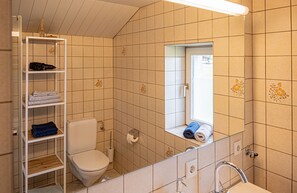 Kylpyhuone, jossa on wc, pyyhkeille tarkoitettu hylly, peili ja ikkuna.
