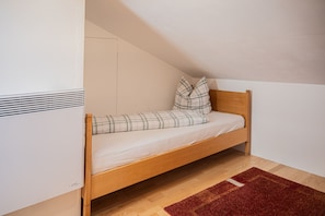 A single bed with a wooden headboard, a red rug, and a white wall with a vent. - Hof 280 - Lingenau Vacation Rentals - Annelies Vacation Rental (Lingenau)