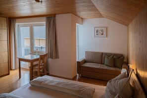 A cozy room with a wooden ceiling, a sofa, a bed, a table, and a window with curtains.