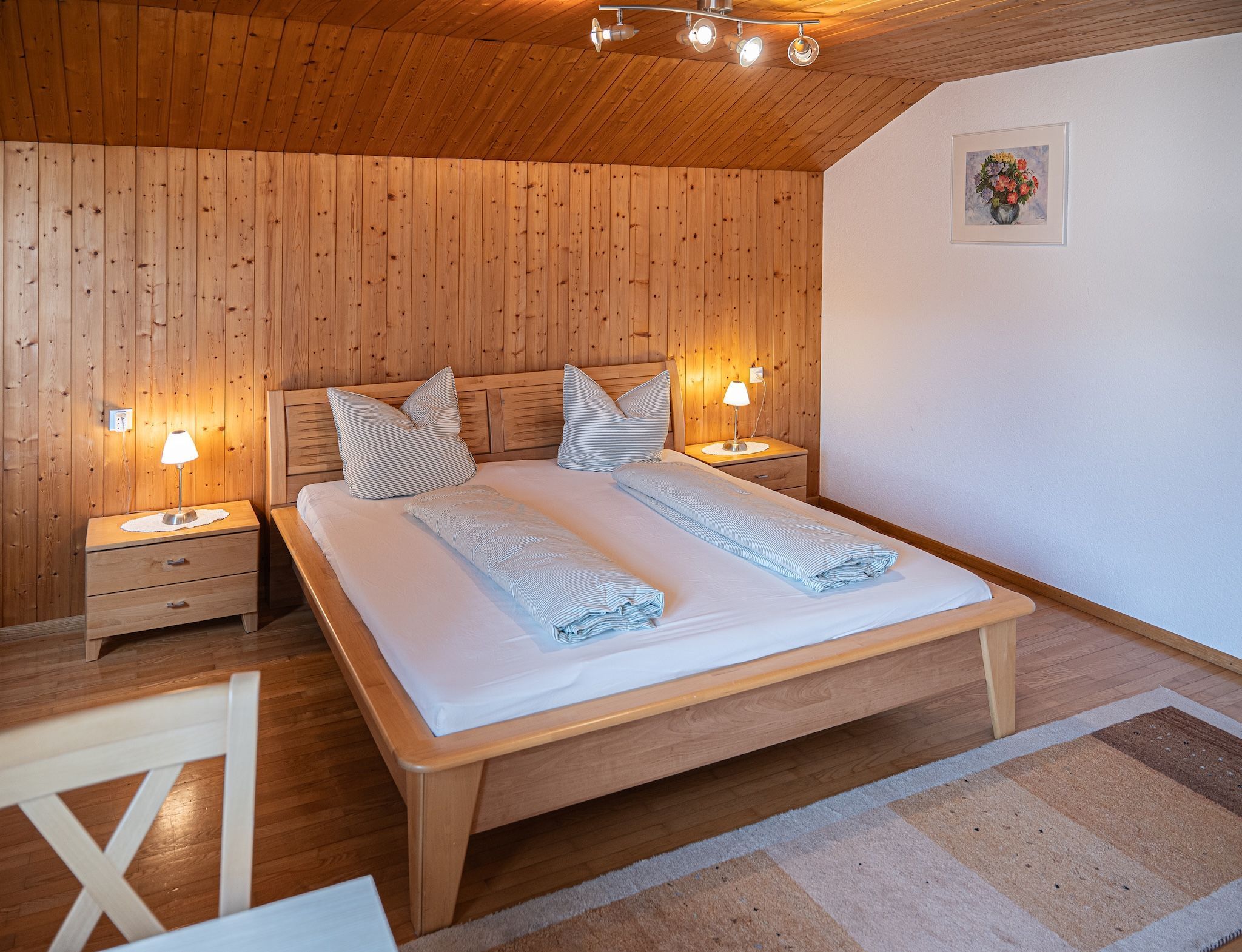 Un dormitorio con paneles de madera, una cama, dos mesitas de noche y una mesilla.