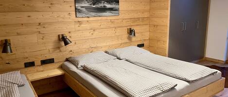 A wooden bed with checkered bedding, a wall-mounted lamp, and a picture of a mountain landscape.