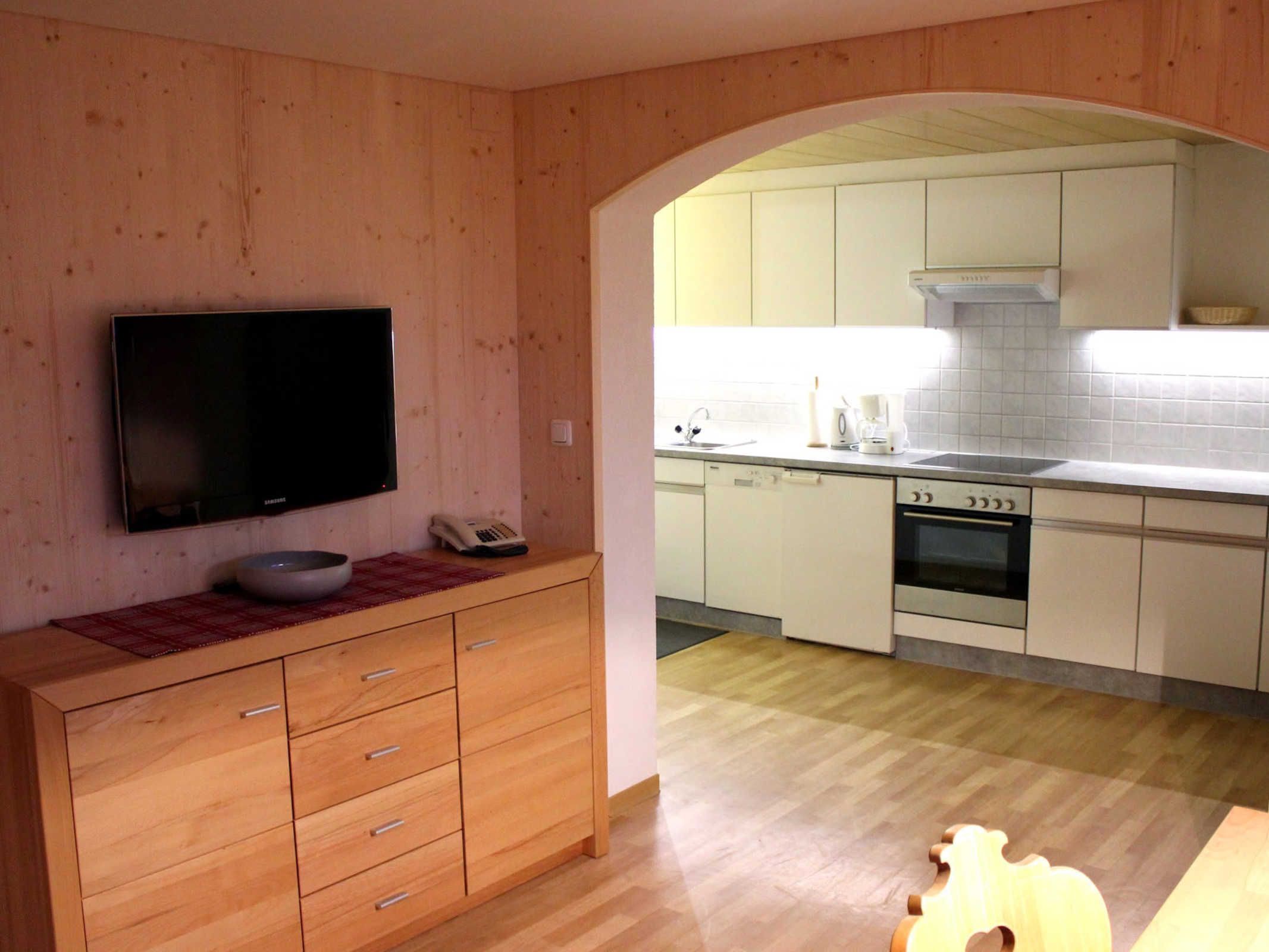 Una cocina moderna con armarios blancos, horno integrado y televisor de pantalla plana montado en la pared.