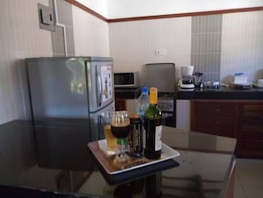Una cocina con refrigerador, microondas y una mesa con una botella y vasos.