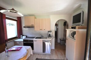 A compact kitchen with a stove, sink, and microwave, wooden cabinets, and a television on a stand. - Vacation apartment cat. 3 1 - Aktiv-Ferienwohnungen Pienz-Bobnar (Sautens)