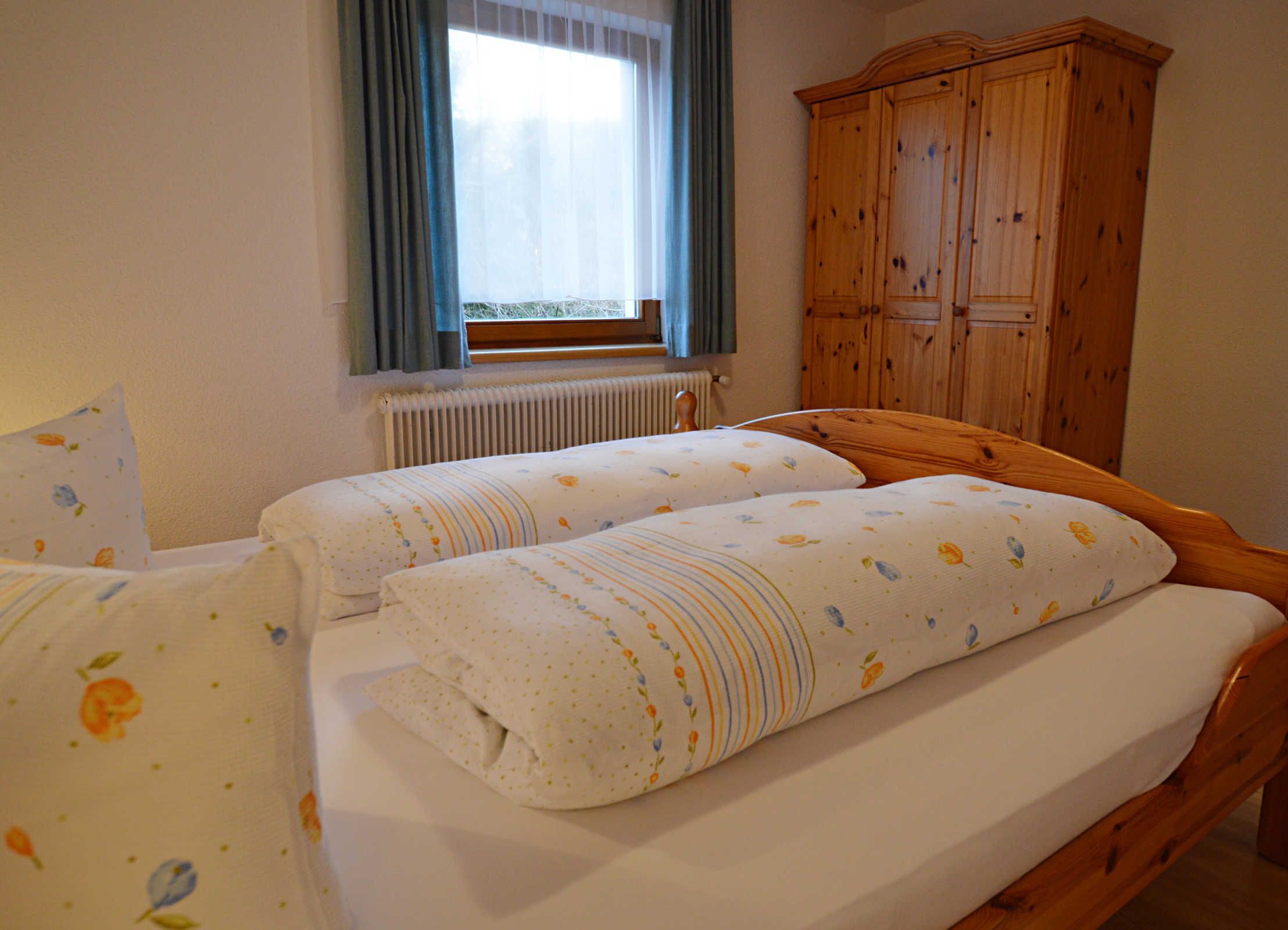 Une chambre avec deux lits, une armoire en bois, une fenêtre avec des rideaux et un radiateur.