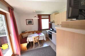 A compact kitchen with a dining table, wooden cabinets, and a window with curtains.