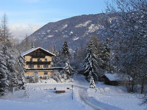 Schneeübersäte Berglandschaft mit einem Chalet, das einen Balkon und eine Holzterrasse besitzt.