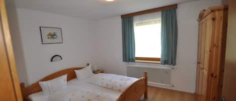 A bedroom with a wooden bed, a radiator, a window with curtains, a framed picture on the wall, and a wardrobe.