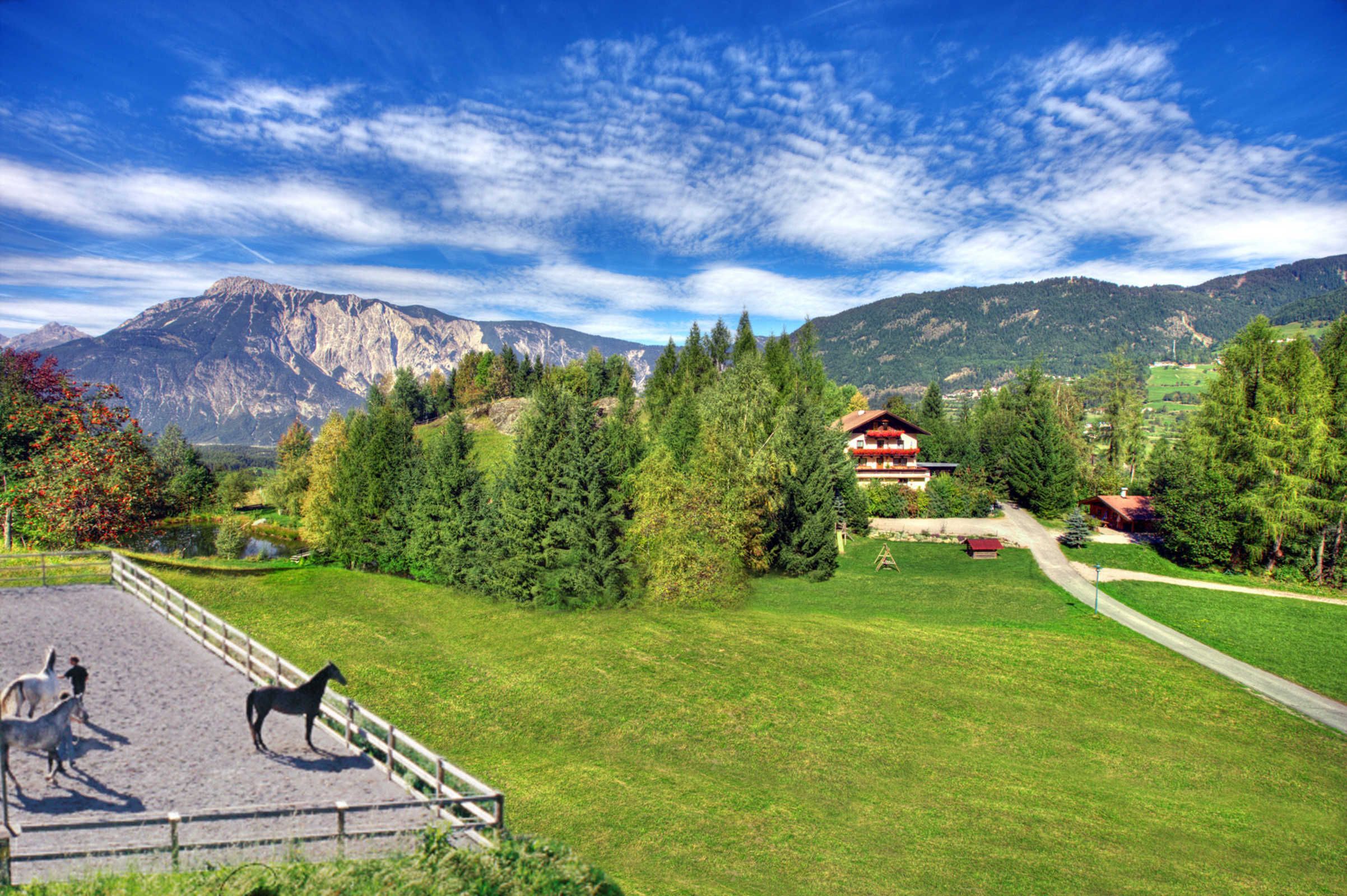 A mountainous landscape with a fenced riding area, a red-roofed building, and a clear sky.